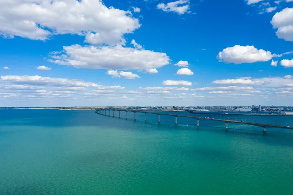 Turkuaz Atlantik suları boyunca uzanan uzun beton köprü dağınık kümülüs bulutlarıyla dolu bir gökyüzünün altında anakarayı Ile de Re 'ye bağlıyor. Geniş deniz manzarası açık kıyı manzarasını ve Charente 'nin sakin atmosferini vurgular.
