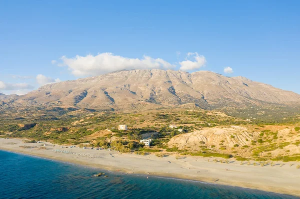 Yunanistan 'ın Girit kentindeki Triopetra plajının hava perspektifi, turkuaz deniz buluşması geniş kumlu sahil ve dramatik kayalık dağlarla açık mavi bir gökyüzünün altında yükseliyor..