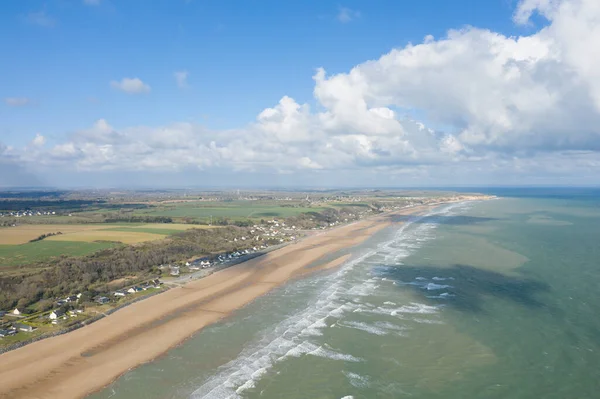 Omaha Sahili 'nin hava manzarası, yumuşak sörf ve yemyeşil tarım arazileriyle çevrili geniş kumlu bir sahil olduğunu gösteriyor. Sahne açık, taze ve huzurlu görünüyor..
