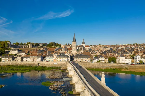 La Charite sur Loire 'ın gelişmiş perspektifi, geleneksel çatıların üzerinde yükselen kendine özgü manastır kulesiyle kasabaya açılan tarihi taş köprüyü gözler önüne seriyor. Loire nehri ve parlak mavi gökyüzü bu klasik Loire Valley sahnesini çerçeveliyor..