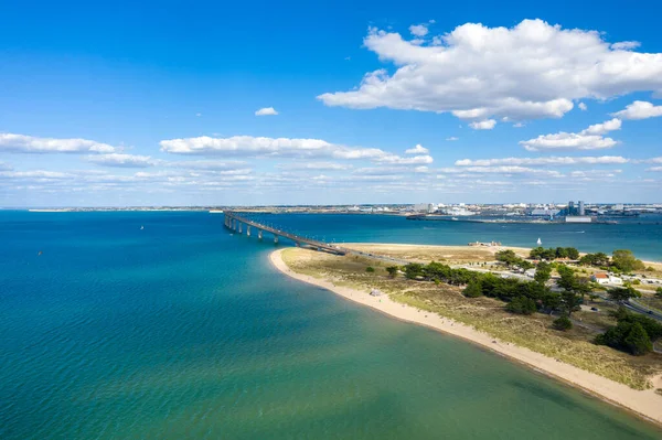 Pont de IIle de Re 'nin kumlu kıyı şeridi, kıyı bitki örtüsü ve dağınık kümülüs bulutlarıyla anakaraya doğru uzanan hava manzarası. Kompozisyon açık deniz manzarası ve sükuneti vurguluyor.