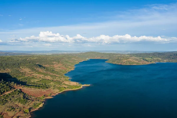 Lac de Salagou 'nun hava perspektifi, yeşil tepeler ve kırmızı dünyayla çevrili, parlak gökyüzü boyunca uzanan dramatik bulutlarla dolu mavi bir kıyı şeridi içeriyor..