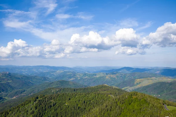 Yuvarlanan orman tepeleri ve Ardeche bölgesinde dramatik beyaz bulutlarla dolu gökyüzünün altındaki uzak mavi dağlar..