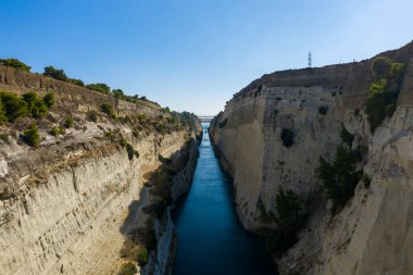 Dik, güneşli kireç taşı uçurumları arasında uzanan parlak mavi suyu olan derin bir kanal. Temiz bir gökyüzünün altında dağınık yeşil çam ağaçları ile kaplı. Dramatik perspektif, sert kaya dokularını ve toprak ve suyun çarpıcı kontrastını vurgular..