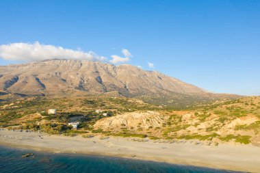 Triopetra, Girit kıyıları boyunca uzanan geniş kumlu sahil, engebeli kayalık dağlar ve açık mavi gökyüzünün altında yükselen dağınık yeşilliklerle kaplı..