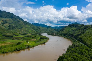Kuzey Laos 'un kırsal kesimindeki dramatik kümülüs bulutları altında gür, ormanlı tepeler arasında geniş bir nehir kıvrılır. Manzara canlı bir yeşilliğe, yuvarlanan dağlara ve canlı bir mavi yaz gökyüzüne sahiptir..