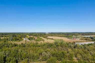 Fransa 'nın orta kesimindeki Imphy yakınlarında açık mavi gökyüzünün altında yeşil tarlaların, dağınık çiftlik evlerinin ve sık ağaçlıkların geniş hava manzarası. Sakin kırsal kesimde açık tarım alanları, yemyeşil bitki örtüsü ve barışçıl bir kırsal atmosfer bulunur..
