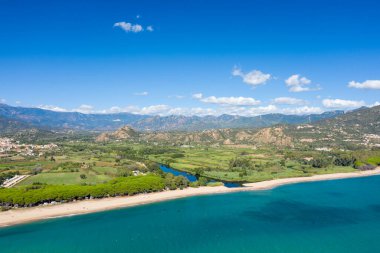 Sardinya 'nın Lotzorai kenti yakınlarında turkuaz deniz bulunan geniş kumlu bir sahile akan dolambaçlı bir nehrin hava manzarası. Bereketli yeşil tarlalar ve uzak dağlar, dağınık bulutlu parlak mavi bir gökyüzünün altında görülebilir..