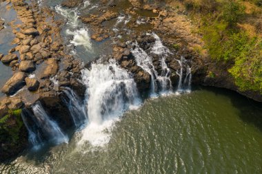 Hava perspektifi, Tad Lo şelalesinin engebeli volkanik kayaların üzerinden Güney Laos 'taki geniş yeşil bir havuza yuvarlanışını yakalar. Güneş ışığı dokuları, akan su, açıkta kalan taş ve kurak mevsim yaprakları arasındaki zıtlığı ortaya koyuyor..