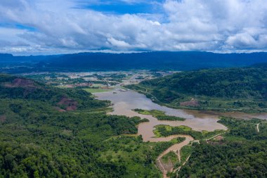 Laos 'un merkezindeki Nam Theun 2 rezervuarının geniş hava perspektifi, yemyeşil tepeler, dolambaçlı su yolları ve dramatik bir gökyüzünün altındaki uzak dağlarla çevrili. Sahne doğal dokuları, su kanallarını ve geniş kırsal bölgeleri vurguluyor.