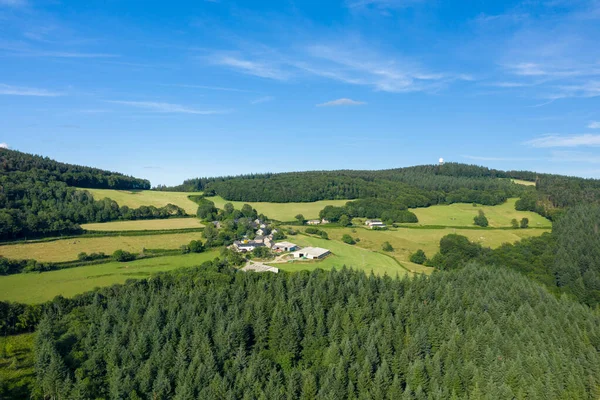 Morvan bölgesinde yemyeşil tarlalar ve yoğun çam ormanlarıyla çevrili küçük bir kırsal köyün havadan görünüşü. Manzara açık mavi bir gökyüzü altında güneşli ve geniştir, sakin bir kırsal atmosfer yaratır..