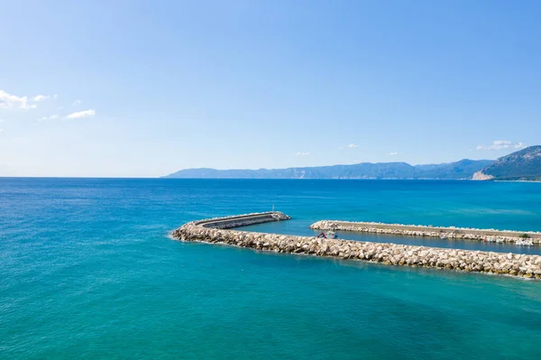 Taştan dalgalar, Orosei kıyı şeridi boyunca berrak turkuaz sulara uzanıyor. Uzak dağlar ve berrak mavi gökyüzü, sakin bir Akdeniz manzarası yaratıyor..
