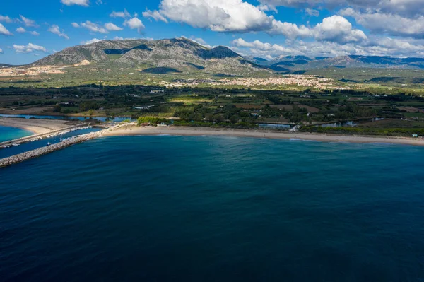 Kumlu sahil ve dalgakıranla buluşan açık mavi deniz manzarası, yemyeşil kırsal ve engebeli dağlar Orosei, Sardunya yakınlarındaki dağınık bulutların altında.