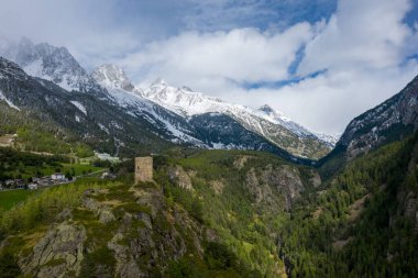 İtalya 'nın Val dAoste şehrinde derin, yeşil tepeleri olan bir vadiye bakan kayalık bir çıkıntının üzerinde ıssız bir taş kule duruyor. Manzara bereketli ormanları, engebeli uçurumları ve Alpler 'in kalbinde dinamik bir gökyüzünü barındırır..