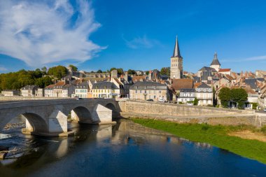 Fransa 'nın orta kesimindeki La Charite sur Loire' ın klasik manzarası, Loire Nehri 'ni geçen tarihi bir taş köprü, rıhtım boyunca geleneksel evler ve canlı mavi gökyüzünün altında yüksek bir kilise kulesi. Nehir kenarı sahnesi ortaçağa ait.