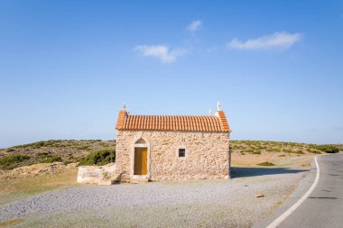 Güneşli Girit kırsalında sessiz, dolambaçlı bir yolun yanında kiremit kaplı, ıssız bir taş şapel duruyor. Basit bina kuru tepeler ve açık gökyüzü ile çevrili, sakin ve izolasyonu çağrıştırıyor..