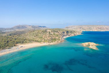 Vai sahilinin geniş hava manzarası, altın kum, turkuaz su ve Girit 'teki güneşli kayalık tepeler. Huzurlu Akdeniz manzarası yemyeşil ve parlak mavi bir gökyüzüne sahiptir..