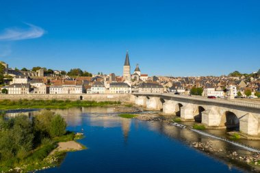 Geniş taş köprü Loire Nehri 'ni geçerek La Charite sur Loire' ın tarihi merkezine doğru uzanır ve kendine özgü manastır kulesi ve canlı mavi gökyüzünün altındaki pastel evleriyle. Berrak yansımalar ve yemyeşil nehir kıyısı bitki örtüsü huzur dolu Loire Vadisi 'ni güçlendirir.
