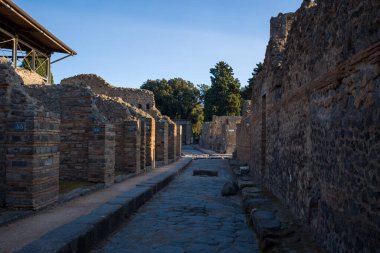 İtalya 'nın Pompeii kentindeki eski Roma sokağı yıpranmış volkanik taş ve tuğla duvarlarla kaplıydı. Yumuşak akşam ışığı yumuşak gölgeler oluşturur. Temiz bir gökyüzünün altında dokulu duvarcılık ve tarihi sokak detaylarını gözler önüne serer..