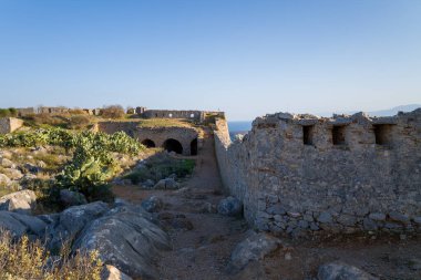 Yunanistan 'ın Nafplio kentindeki Palamidi Kalesi' nde dikenli armut kaktüsüyle kaplı kayalık bir yamaç boyunca eski taş kale duvarları uzanıyor. Sıcak öğleden sonra ışığı, açık mavi gökyüzünün altındaki dokulu ve kurak Akdeniz manzarasını vurgular..