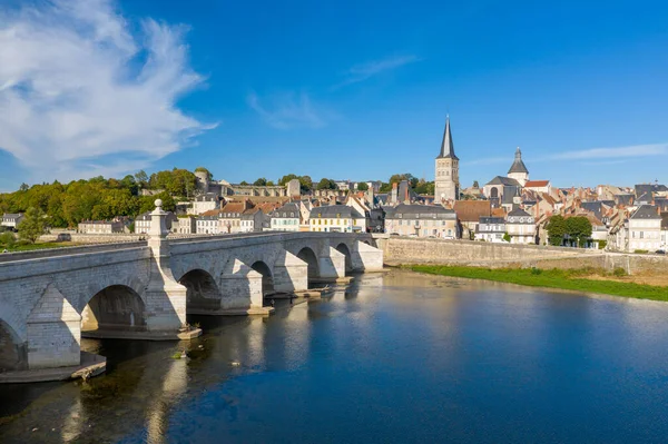 Fransa 'nın orta kesimindeki La Charite sur Loire' ın klasik manzarası, Loire Nehri 'ni geçen önemli bir taş köprü, ortaçağ çatıları ve canlı mavi gökyüzünün altında uzun bir kilise kulesi. Nehir kenarı manzarası miras mimarisi ile zenginliği harmanlıyor.
