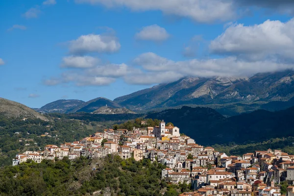 Rivello, İtalya 'nın verimli bir yamacında, canlı mavi gökyüzü ve dağılmış bulutların altında engebeli dağ yamaçları olan terakotta çatılı evler bulunuyor. Gıcır gıcır gün ışığı zengin dokular ve doğal renkler ortaya çıkarır..