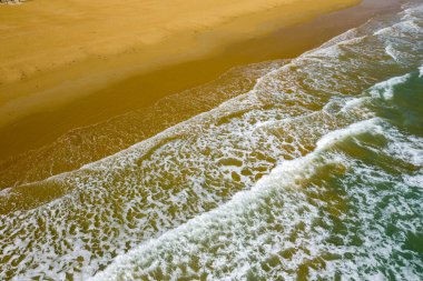 İtalya 'nın Apulia kentindeki Vieste sahilinin geniş altın kumu üzerinde süzülen yumuşak köpüklü dalgaların havadan bakış açısı. Sahne, yumuşak gün ışığında çekilen suyun oluşturduğu dokulu kıyı şeridini ve doğal desenleri vurguluyor..