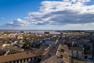 Ortaçağ taş duvarları ve pembe tuz bataklıkları ile dağılmış bulutlarla dolu dramatik bir gökyüzü altında Aigues-Mortes teras çatıları üzerinde geniş görüş.
