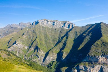 Sivri yeşil ve kayalık tepeler, Gavarnie Gedre yakınlarındaki Pireneler 'de güneşli bir dağ yamacında dramatik gölgeler bıraktı. Açık mavi gökyüzü çarpıcı kontrastı ve engebeli alp dokusunu artırır.