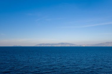 Geniş bir derin mavi su, berrak mavi bir gökyüzünün altındaki uzak dağlık bir kıyı şeridine doğru uzanıyor. Sahne, Adriyatik bölgesinin sakin atmosferini ve asgari bileşimini yakalıyor.