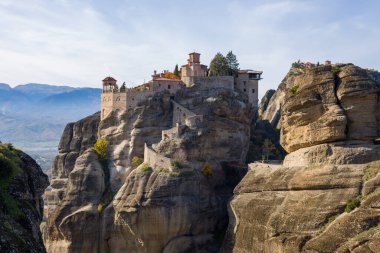 Varlaam Manastırı, Yunanistan 'ın Meteora kentindeki yüksek kumtaşı oluşumlarının tepesinde, güneş ışığı ile dağlık bir zemin üzerindeki desenli kaya ve terracotta çatıları vurgulanıyor..