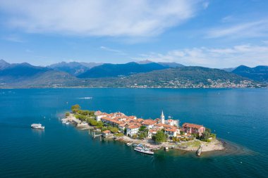 Isola dei Pescatori 'nin yüksek açılı perspektifi, terracotta çatıları, kilise kulesi ve Maggiore Gölü' nün mavi sularıyla çevrili canlı rıhtımı. Orman dağları ve göl kenarındaki yerleşim yerleri kuzeyde manzaralı bir dağlık zemin sağlar.