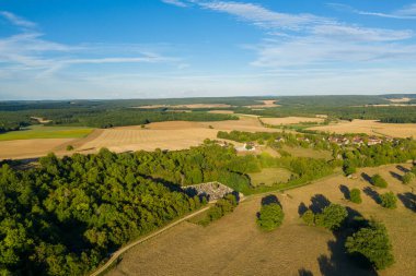 Cuncy les Varzy köyünün geniş hava manzarası. Etrafı yamalı tarlalarla, sık ağaçlıklarla ve parlak mavi bir gökyüzü altında yuvarlanan tepelerle çevrili. Kırsal alanda dağınık evler, altın tarlalar ve Burgundy 'deki yemyeşil alanlar yer almaktadır.