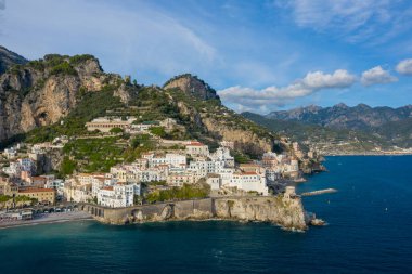 Geniş bir manzara, İtalya 'nın Amalfi kentindeki güneşte yıkanmış binaları yakalıyor ve derin mavi Akdeniz' e doğru dik kayalıklardan aşağı yuvarlanıyor. Dramatik kıyı şeridinde tarihi taş kemerler, gür yeşillikler ve berrak bir gökyüzünün altında engebeli dağlar yer alıyor..