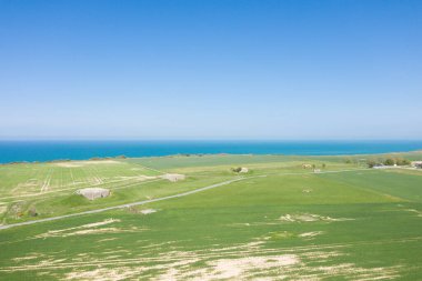 Normandiya 'nın Longues-sur-Mer kentindeki mavi denize bakan tarihi 2. Dünya Savaşı sığınaklarıyla kaplı geniş bir yeşil alan manzarası. Açık gökyüzü ve açık arazi barışçıl ve geniş bir atmosfer yaratır..