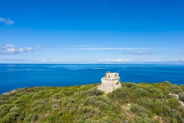 Isola di Cirella 'daki yemyeşil bitki örtüsünün üzerinde yükselen tarihi taş kule, durgun masmavi deniz ve açık gökyüzü çarpıcı bir kıyı manzarası yaratıyor. Parlak güneş ışığı, eski yapının ve çevreleyen doğanın dokusunu vurgular..