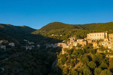 Pisciotta 'nın geleneksel binaları, sık ormanlık ve açık mavi gökyüzü olan yemyeşil bir yamaçta tünemiş sıcak akşam güneşinin tadını çıkarırlar..