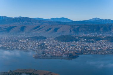 Geniş bir hava perspektifi, Yunanistan 'ın Epirus kentindeki Pindus dağlarının engebeli zimine kurulmuş Ioannina Gölü' nün göl kenti ve etrafındaki sakin suları içine alır. Suyun üzerinde hafif bir sis sürükleniyor.