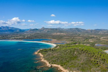 Sardinya 'daki Spiaggia Lu Impostu' nun havadan görünüşü turkuaz su, beyaz kumlu yay ve dağınık mavi bulutların altında yemyeşil tepeler ile süpürülen bir körfezi vurguluyor..
