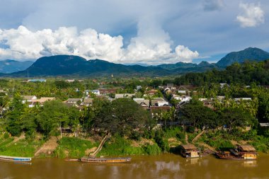 Geleneksel çatıları, yemyeşil yeşilliği ve ön plandaki kahverengi Mekong Nehri ile Luang Prabang 'ın manzarası yükseldi. Orman dağları ve dramatik kümülüs bulutları parlak gün ışığında çarpıcı bir zemin oluşturur..