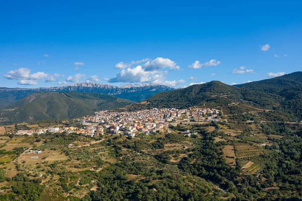 Yuvarlanan tepeler, zeytinlikler ve Sardunya 'da dağınık bulutlarla dolu mavi bir gökyüzünün altındaki dramatik dağ sırtlarıyla çevrili Orgosolo' nun hava manzarası..