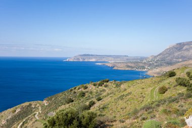 Yunanistan 'ın Vathia kenti yakınlarındaki açık mavi bir denize doğru uzanan yeşil tepelerin geniş manzarası. Engebeli arazisi ve berrak gökyüzünün altındaki uzak kıyı şeridi olan güneşli bir manzara..