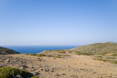 Girit 'te berrak bir gökyüzünün altında canlı mavi Akdeniz manzaralı geniş kayalık plato. Nadir bitki örtüsü ve engebeli tepeler bir açıklık ve sükunet hissi yaratır..