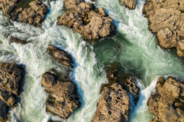 Laos 'un güneyindeki Mekong Nehri' ndeki Chutes de Khone 'daki engebeli kayalar arasında dalgalanan beyaz su akıntılarının ayrıntılı hava görüntüsü. Dönen su, taşın dokusuyla çelişiyor. Şelalenin dinamik şablonlarını vurguluyor..