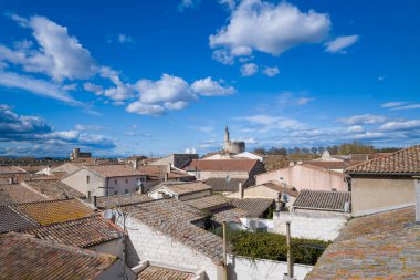 Yıpranmış terasotta kiremitleri olan köyün çatıları Aigues-Mortes 'deki dramatik bulutlarla dolu canlı mavi gökyüzünün altında tarihi bir taş kuleye doğru uzanıyor..