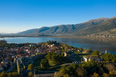 Erken güneş ışığı, Yunanistan 'ın Epirus kentindeki Pindus dağlarının eteklerini yansıtan Ioannina Gölü ile tarihi kaleyi, kırmızı kiremitli çatıları ve ağaçlarla kaplı caddeleri aydınlatıyor. Sahne sakin bir göl havası yakalıyor ve...