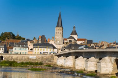 Sivri uçlu manastır kulesi, orta çağ mimarisini yansıtan berrak mavi gökyüzü ve durgun nehir suyuyla Pastel evler ve La Charite sur Loire 'nin taş köprüsünün üzerinde yükselir. Güneşli cepheler ve geleneksel çatılar bu karakterin altını çiziyor