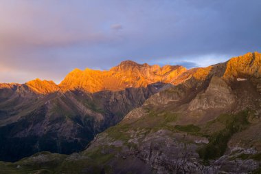 Canlı turuncu güneş ışığı, alacakaranlıkta Pireneler 'in engebeli dağ zirvelerini yıkar dramatik kaya dokularını ve renkli bir akşam gökyüzünün altındaki derin vadileri aydınlatır..