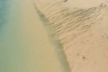 İngiliz Manş Denizi kıyı şeridi drone görüntüsü açık gün ışığı altında sığ turkuaz suyu birleştiren karmaşık kum dokularını ve nazik dalgaları ortaya koyuyor..