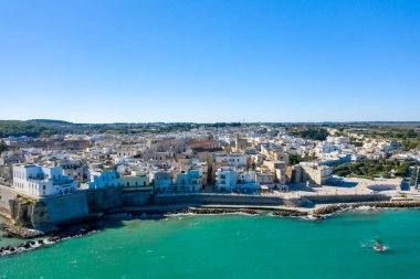 Canlı turkuvaz Adriyatik Denizi 'ni kaplayan beyaz boyalı binalar ve taş duvarlarla dolu tarihi Otrantos manzarası. Sahne, kıyı mimarisi, açık mavi gökyüzü ve güney İtalya 'nın eşsiz karakterini ön plana çıkarıyor..